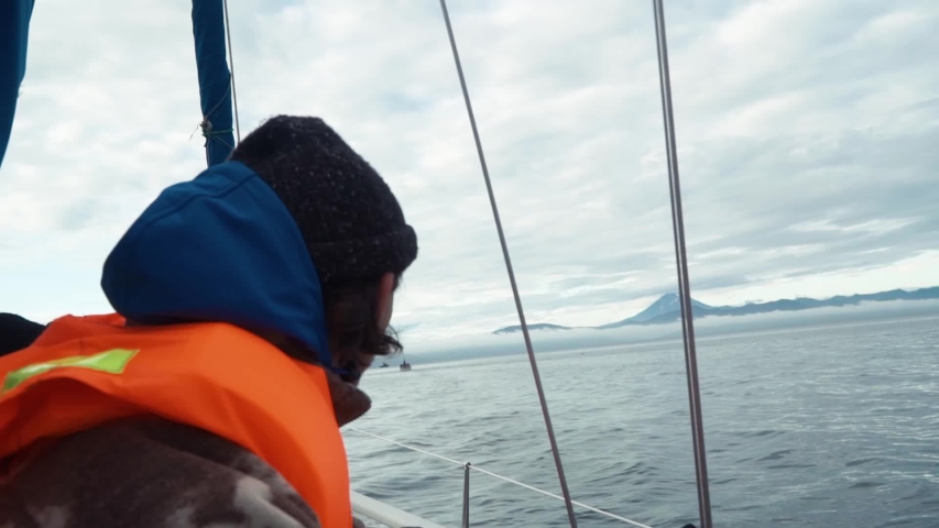 Tourist in a life jacket on boat. Vilyuchinsky volcano (also called Vilyuchik) is visible in the background. Kamchatka