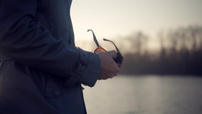 Man Cleaning Sunglasses At Sunset.Hand Cleaning And Polished Sunglasses Lens Using Cloth. Close Up Man Rubs Glasses With Black Rag.