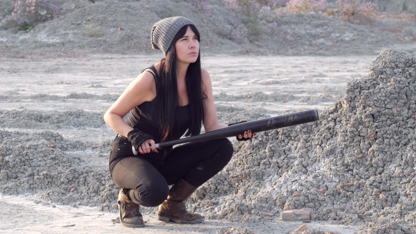 Sexy bold hipster girl tomboy sits in a vacant lot with a baseball bat