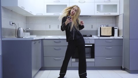 Young woman use phone while dancing singing in kitchen at home in the morning pajamas smiling attractive fun happy home beautiful enjoyment dance happiness entertainment slow motion