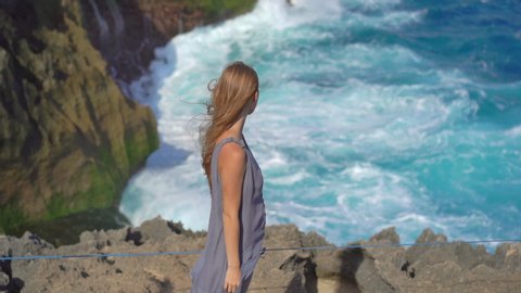 Young woman tourist visits the Angel's Billabong beach at the Nusa Penida island where huge waves are breaking on the rocks. Slowmotion shot