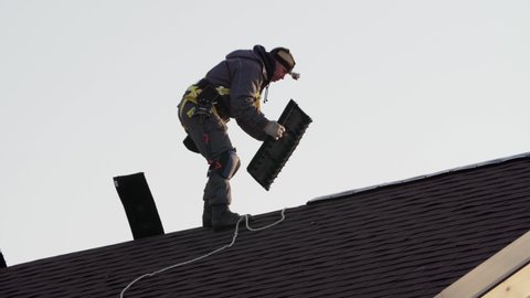 Tiler in safety harness is making roof ridge. Works at height. Frame house under construction