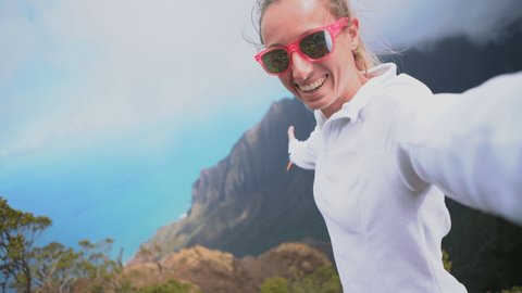 Young woman on a hike in Hawaii takes cool selfie from mountain top overlooking Pacific Ocean 