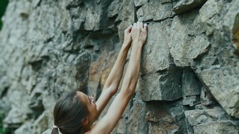 young slim muscular woman rockclimber climbing on tough sport route, searching, reaching and gripping hold. climber makes a hard move. outdoors rock climbing and active lifestyle, slow motion climbing