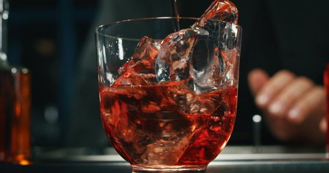 Close up of a professional bartender is preparing an alcoholic cocktail with professional crystal long lasting ice cubes to customers at the bar or disco club.