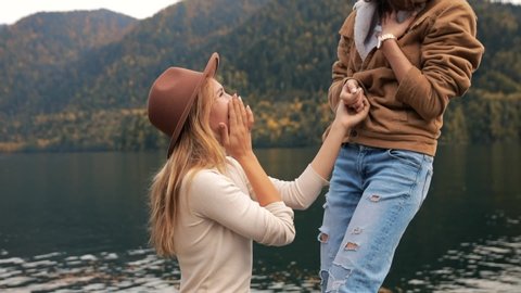 two lesbians make an offer to get married and agree, attractive young women fashionably dressed on vacation on a lake in the mountains. lgbt, gay, same-sex marriage, equal rights concept.