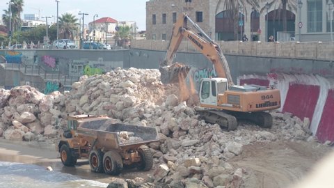 Tel Aviv - December 4th 2019: Construction work at a city beach, by the old Jaffa port. Excavator loading a dump truck with dirt to clear away.