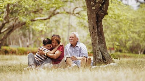 Old people, senior couple, elderly man and woman, husband and wife in park, active seniors, retirement age. Outdoor family fun. Happy grandpa and grandma hugging boy, child, kid at picnic. Slow motion