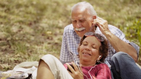 Old people, senior couple, elderly man and woman, husband and wife in park, retired seniors. Outdoors activity, leisure, fun, recreation. Grandpa and grandma listening to song, music with mp3 player 