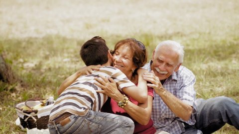 Old people, senior couple, elderly man and woman, husband and wife in park. Outdoors activity, leisure, family recreation. Happy grandfather and grandmother hug grandson, boy, child. Slow motion 