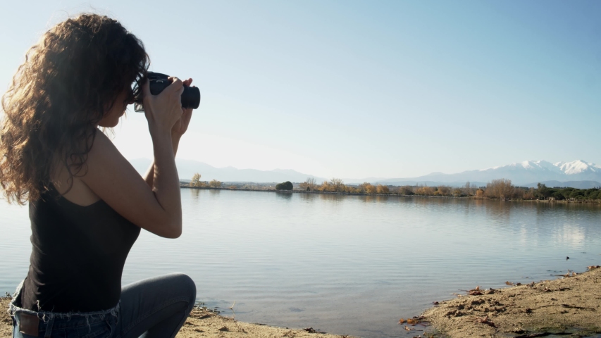 Woman photographing landscapes on a lake taking pictures with a reflex camera