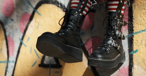 Slow motion goth teenager girl slide with rough boots striped stockings sits on ornate wall of an abandoned building. Alternative in youth. An alternative in youth. Hipster, freak, emo, grunge. Copy 