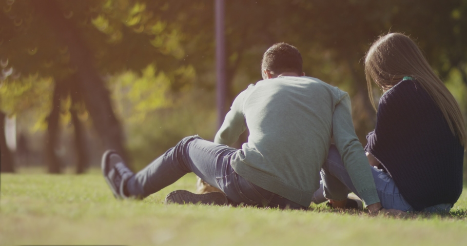4K Back view of happy lovely caucasian romantic couple sitting on lawn and hugging each other in park . Rear view of young couple sit on grass and enjoy in the open air. Happiness people. Slow Motion. | Shutterstock HD Video #1042623091