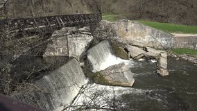 Retro derelict wooden bridge over river waterfall cascade water flowing. Static shot. 4K UHD video clip.