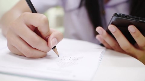 Girl student holding pen and writing in notebook. Close up,And use the phone 