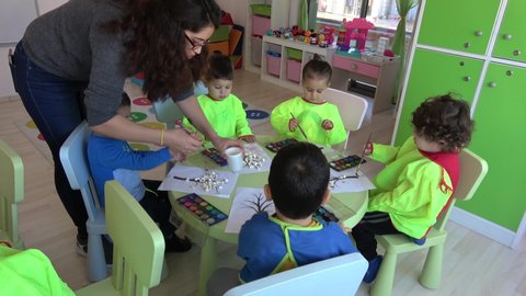 Fethiye, Turkey - 28th of November 2019: 4K At the Istanbul Development nursery school - Teacher helps three years old children to master painting 
