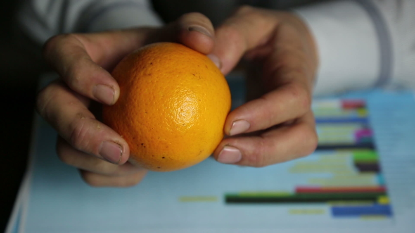 Hands with orange over sales growth graph.
Farmer businessman considers the profits and expenses of the harvest of oranges.
