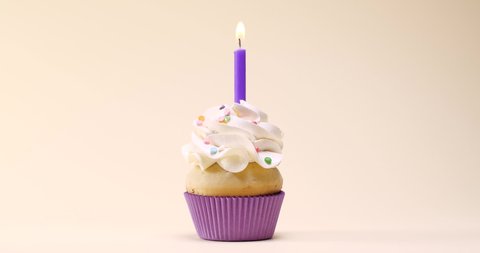 Delicious birthday cupcake with burning candle on beige background. Slow motion effect Arkistovideo