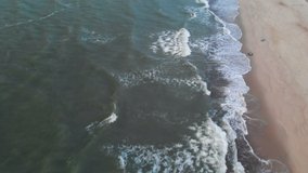Aerial view of a low key A video about a tropical beach at blue hour after sunset showing evening footage of green foaming ocean waves crashing onto the coastline. Top view without people