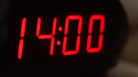 Close-up of black digital clock screen showing 14.00. Blinking red digital numbers on black background. Modern timer system and neon light, electric alarm device