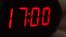 Close-up of black digital clock screen showing 17.00. Blinking red digital numbers on black background. Modern timer system and neon light, electric alarm device