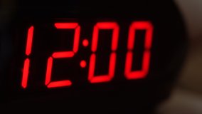 Close-up of black digital clock screen showing 12.00. Blinking red digital numbers on black background. Modern timer system and neon light, electric alarm device