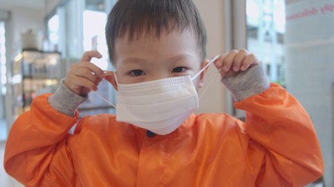 Cute little Asian 3 - 4 years old toddler boy child wearing / put on protective medical mask against bacteria and viruses by himself