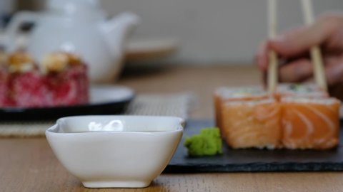 Delivery food concept: somebody dips philadelphia rolls sushi into soy sauce, close up