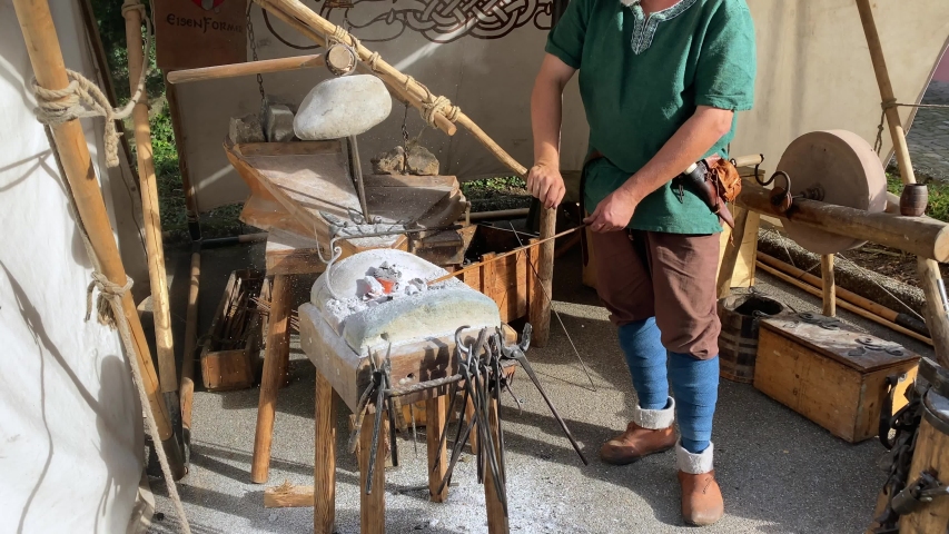 Medieval man blowing air on fireplace to get burning heat to forge equipment,static