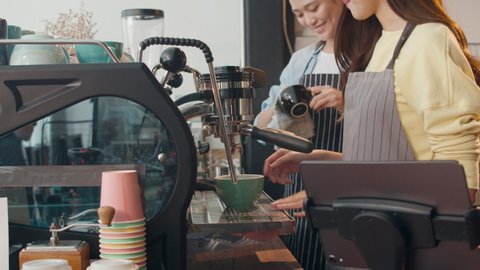 Beautiful young Asia lady barista working with coffee machine in coffee shop. Two small business owner Korean girl in apron making coffee by coffee machine with friend at counter in urban cafe.