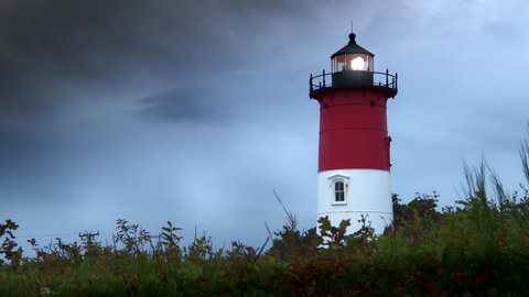Classic view of an Atlantic Ocean coastal lighthouse at dusk. Gloomy gray weather and cloudy skies. Light beam shines out into the misty sky.