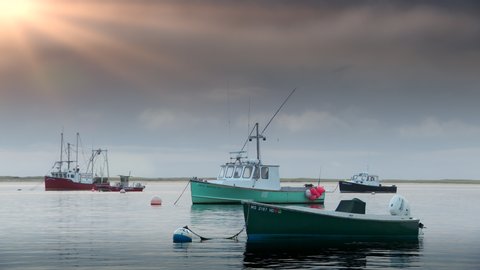 Cape Cod, MA circa October 2019: Classic scene of a lobster fishing boat moored in a cove at sunset in Chatham harbor on Cape Cod in Massachusetts. Seagulls and birds fly overhead.