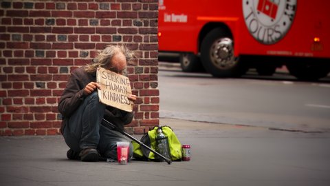 BOSTON, MA - circa 2019: Homeless man begging on city street holding sign that says SEEKING HUMAN KINDNESS. Many people walk past the poor man on the sidewalk without offering to help.