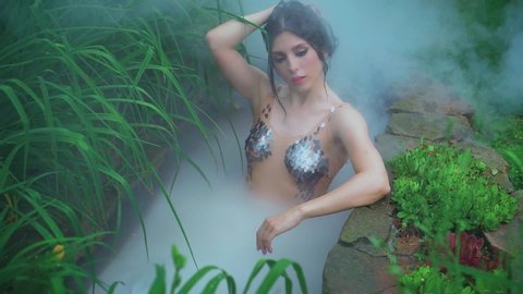 young sexy body woman bathes steamy hot springs water touches wet dark hair. Natural beauty pretty face style queen Cleopatra. creative silver scale swimsuit. Fairy Fashion shoot with nitrogen dry ice