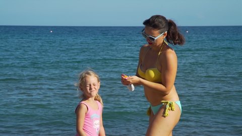 Young Mother Putting Sunscreen on Face of her Daughter on the Beach in Slow Motion. Children Healthcare and Sun Protection at Travel Time Concept