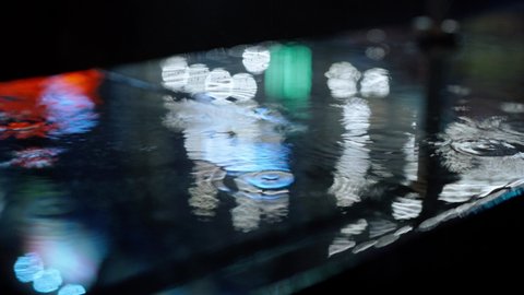 closeup Rain drops Falling On puddle with lights reflection on city sidewalk. Rain Drop With Street Lights and colorful traffic lights At Night Blur Bokeh Abstract 4k stock footage