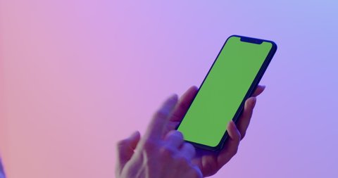 MINSK/BELARUS - CIRCA 2019: GREEN SCREEN CU Caucasian female using iPhone XS Max, vertical orientation, colorful neon background. 4K UHD RAW Graded footage