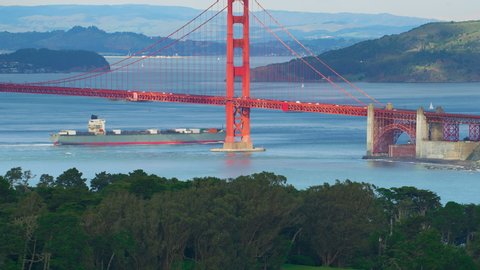 Aerial view of the magnificent Golden Gate Bridge with a cargo ship passing under it. This bridge connects the San Francisco peninsula to Marin County. US route 101 and SR 1 full of cars. Red 8K.