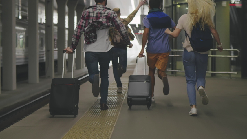 Back view of four friends passengers running along train platform being late. Tourist group missing train and trying to chase it. Four people running after train. | Shutterstock HD Video #1042707652