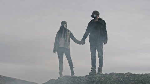 A survivor lovely couple in gas mask joining hands together on desolate out landscape.