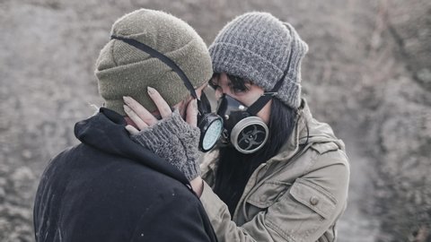 A survivor lovely couple in gas mask hugging on desolate out forest landscape.
