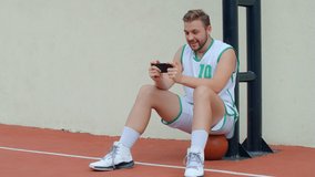 Basketball Fan Reaction Concept - Excited basketball player in basketball outfit watching his favourite team on smart phone, 4k slow motion