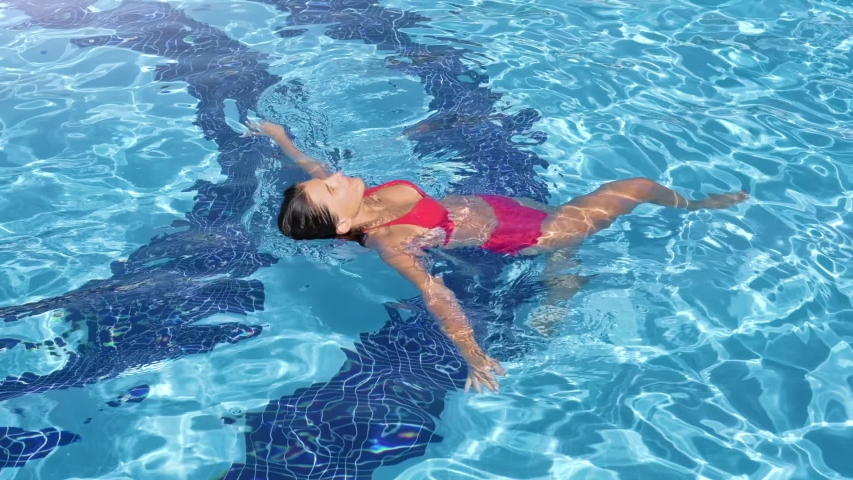 Relaxed woman in bikini swims in swimming pool surrounded by clear bright water slow motion | Shutterstock HD Video #1042723906
