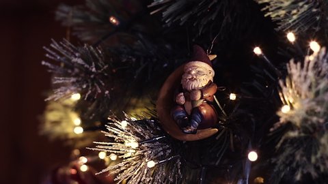 A Santa Claus ornament hangs in a Christmas tree with lights fading on and off.
