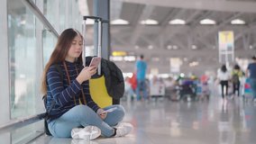 4K handheld clip with young pretty girl sitting on the floor of airport, she use smartphone and look around for find, then she place shin on hand with feeling bore to waiting