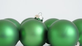 Matte green color Christmas baubles on white 4K tilting video