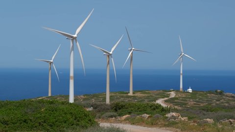 CRETE ISLAND, GREECE - MAY 19, 2019: Green renewable alternative energy concept - wind generator turbines generating electricity. Wind farm on Crete island, Greece with small white church