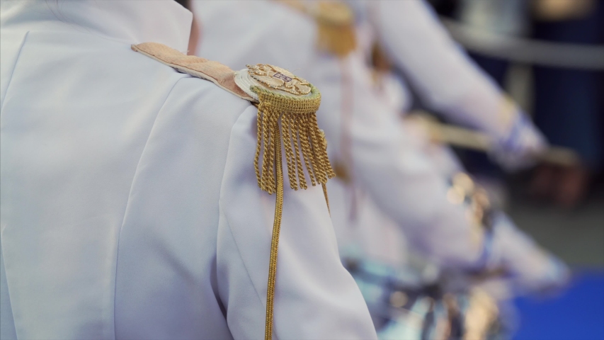 Close view of decorative epaulets on female drummer shoulder. Band of ladies drummers in white costumes play drum