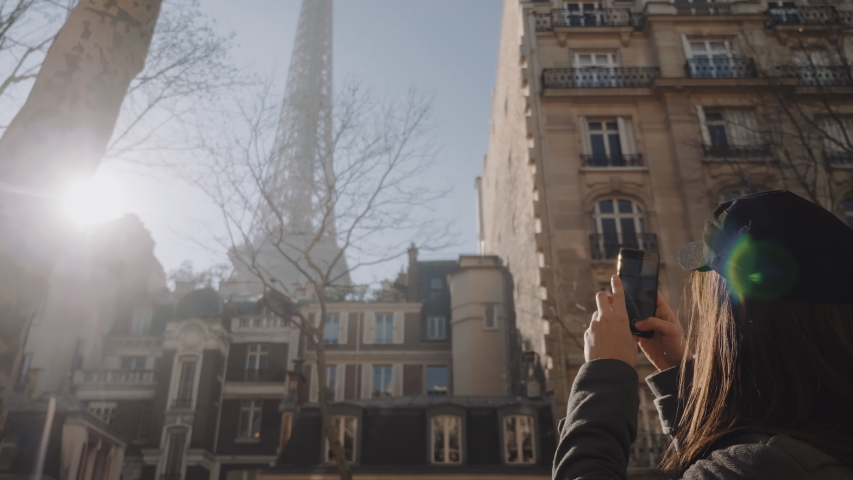 Happy beautiful tourist woman taking smartphone photo of Eiffel Tower on Paris vacation, amazing lens flare slow motion.