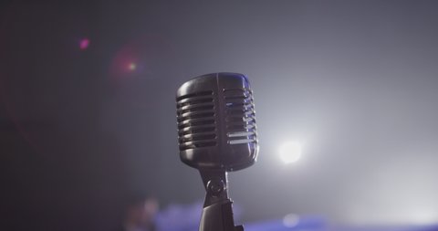4K Few shots of professional concert vintage glare microphone for record or speak to audience on stage in dark empty retro club close up.  Vintage microphone against a dark background with spotlight .